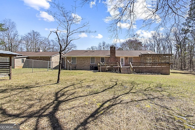 rear view of house with fence, a wooden deck, a yard, a chimney, and brick siding