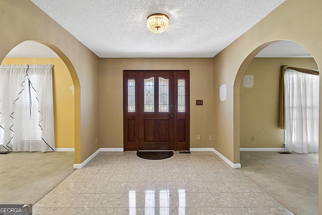 foyer featuring light tile patterned floors, baseboards, light colored carpet, and a textured ceiling