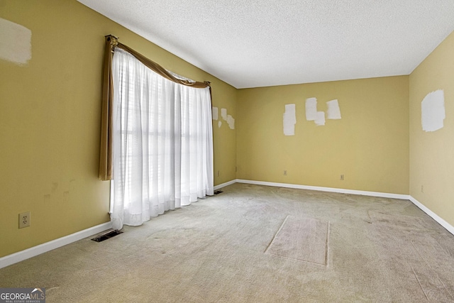 carpeted empty room featuring visible vents, a textured ceiling, and baseboards