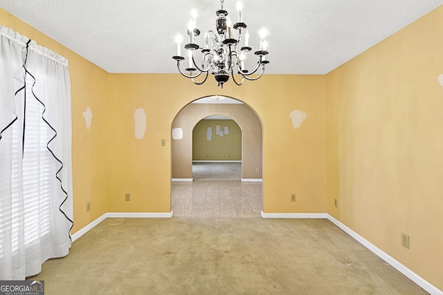 unfurnished dining area with baseboards, arched walkways, a textured ceiling, and carpet flooring