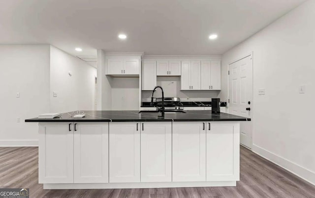 kitchen featuring a sink, wood finished floors, a center island with sink, and white cabinetry