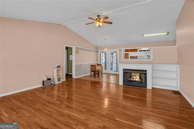 unfurnished living room with wood finished floors, a multi sided fireplace, ceiling fan, vaulted ceiling, and french doors