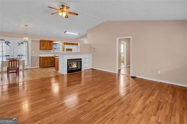 unfurnished living room featuring lofted ceiling, light wood-style floors, a lit fireplace, baseboards, and ceiling fan