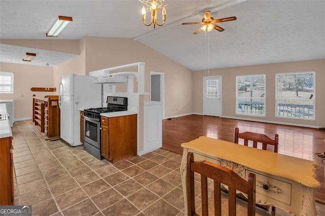 kitchen with tile patterned flooring, stainless steel range with gas cooktop, lofted ceiling, brown cabinets, and freestanding refrigerator