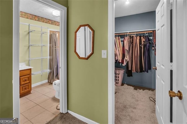 interior space with tile patterned floors, a walk in closet, baseboards, and toilet