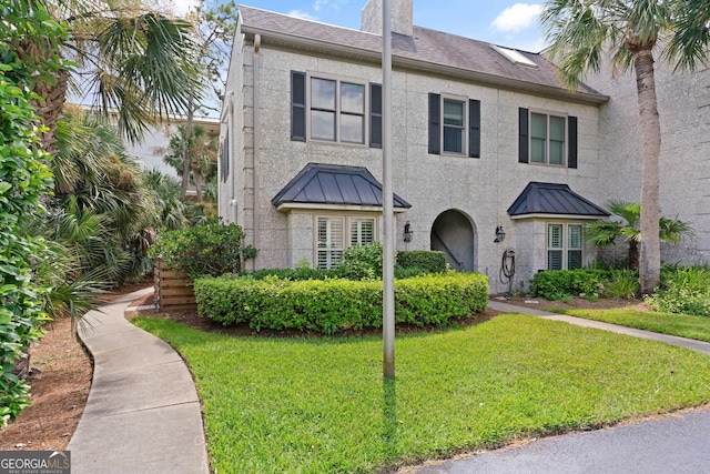 townhome / multi-family property featuring a standing seam roof, a front lawn, metal roof, and stucco siding