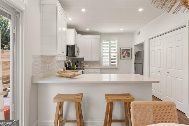 kitchen featuring backsplash, appliances with stainless steel finishes, a peninsula, and light countertops