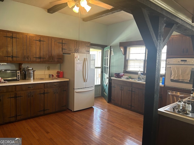 kitchen with light wood finished floors, beamed ceiling, a toaster, light countertops, and white appliances