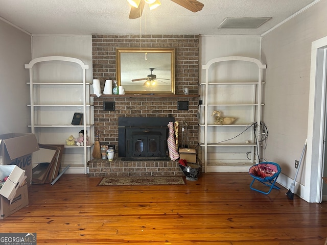 unfurnished living room featuring visible vents, a wood stove, hardwood / wood-style flooring, a textured ceiling, and a ceiling fan