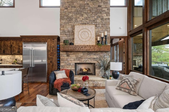 living area featuring a warm lit fireplace, dark wood-type flooring, and a high ceiling