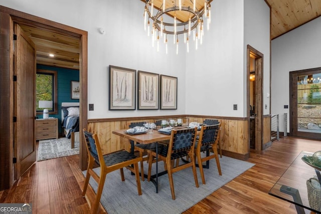 dining room with a notable chandelier, wood finished floors, wood walls, wainscoting, and a towering ceiling