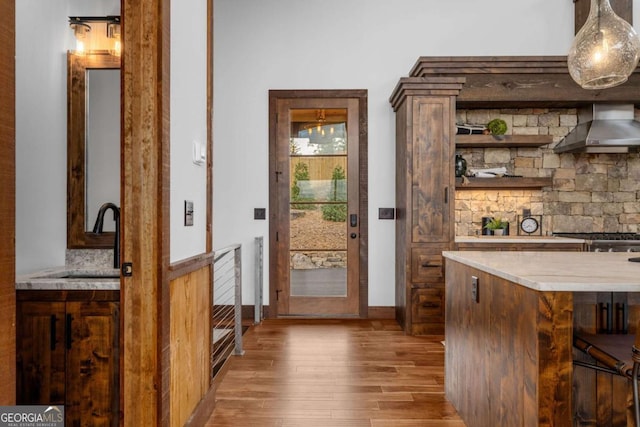 bar with decorative light fixtures, light wood-style floors, wall chimney range hood, and a sink