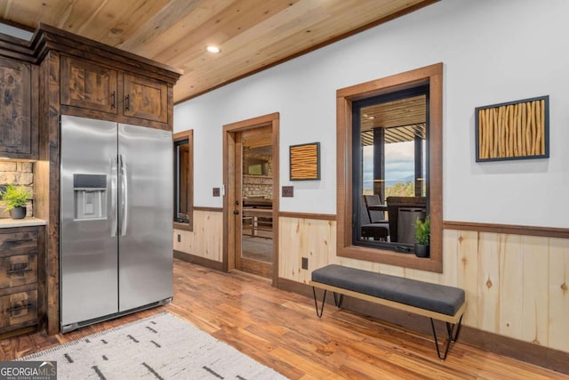 kitchen with a wainscoted wall, light wood-style flooring, dark brown cabinetry, stainless steel fridge with ice dispenser, and wood ceiling