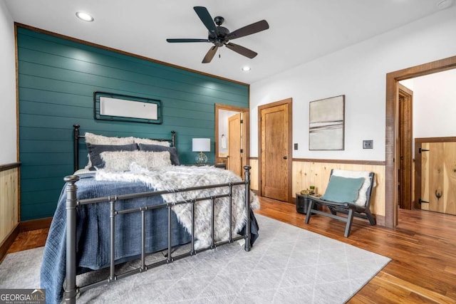 bedroom featuring wooden walls, ceiling fan, recessed lighting, wainscoting, and wood finished floors