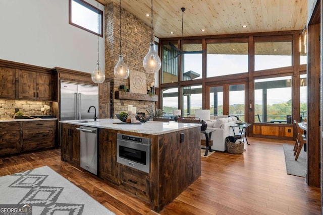 kitchen with appliances with stainless steel finishes, light countertops, an island with sink, and dark wood-style flooring