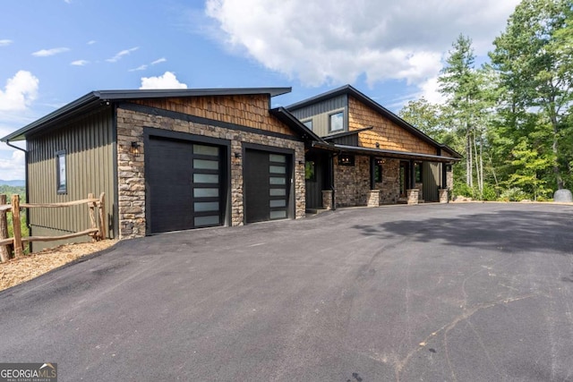 view of front of house with aphalt driveway, stone siding, a garage, and fence