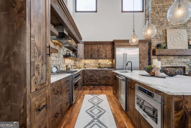 kitchen with wall chimney range hood, dark wood finished floors, decorative light fixtures, premium appliances, and decorative backsplash