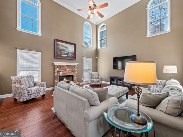 living room with ornamental molding, a ceiling fan, a fireplace, baseboards, and dark wood-style flooring