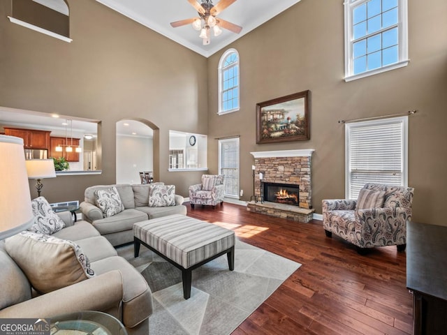 living room with baseboards, ceiling fan, a stone fireplace, arched walkways, and dark wood-style flooring