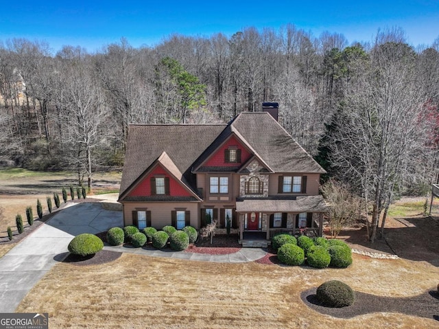 view of front facade with a chimney, covered porch, driveway, and a forest view