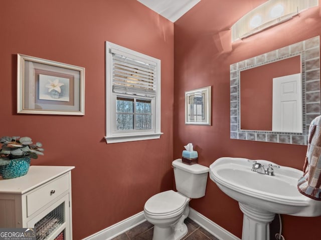 half bath with tile patterned floors, toilet, baseboards, and a sink