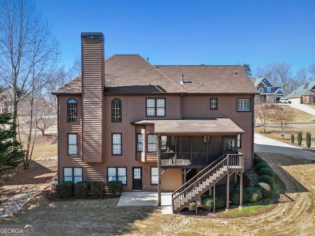 rear view of house with a shingled roof, stairway, a chimney, a sunroom, and a patio area