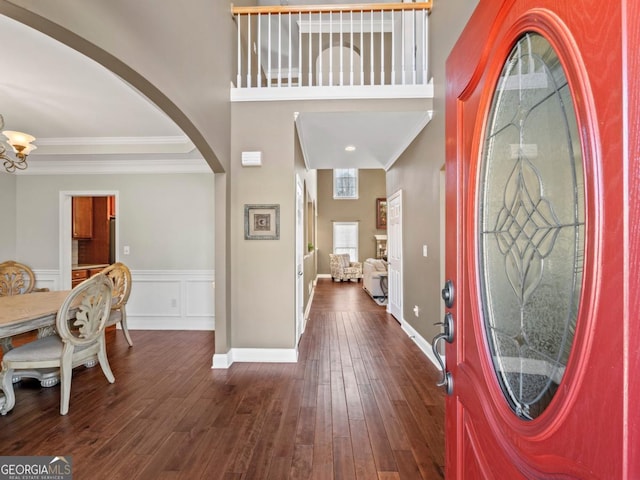 entryway with crown molding, dark wood-style floors, wainscoting, an inviting chandelier, and arched walkways