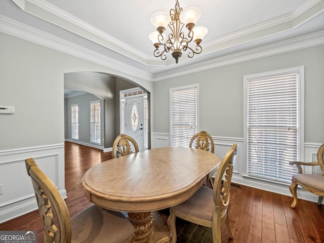 dining room featuring a wainscoted wall, arched walkways, a healthy amount of sunlight, and hardwood / wood-style flooring