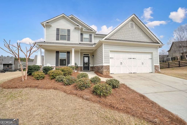 craftsman-style house featuring driveway, stone siding, fence, covered porch, and an attached garage