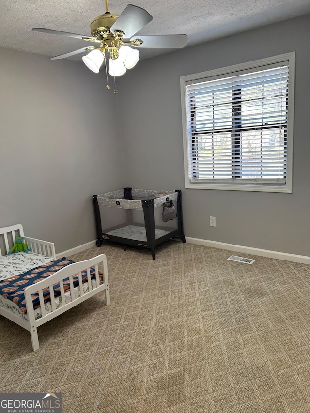 carpeted bedroom featuring visible vents, baseboards, a textured ceiling, and a ceiling fan