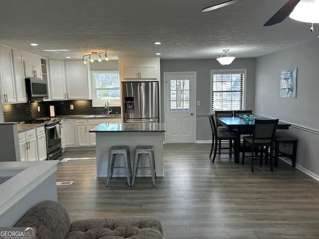 kitchen featuring dark wood-type flooring, backsplash, a center island, stainless steel appliances, and white cabinets