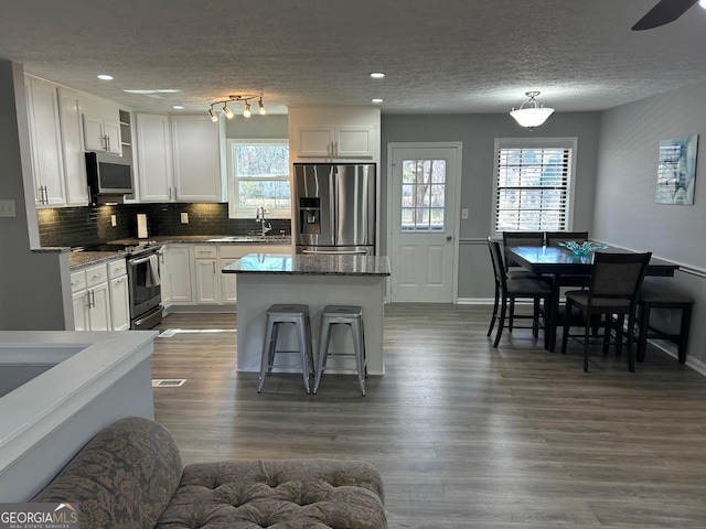 kitchen featuring dark wood-type flooring, tasteful backsplash, a center island, appliances with stainless steel finishes, and white cabinets