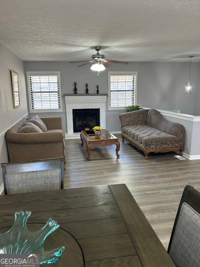 living area with a brick fireplace, plenty of natural light, wood finished floors, and a textured ceiling