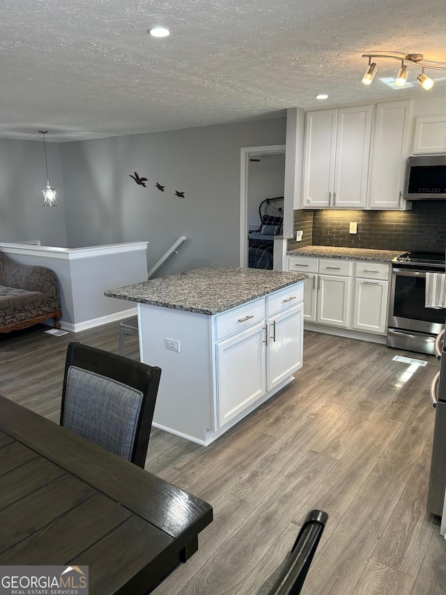 kitchen with wood finished floors, stone countertops, stainless steel appliances, white cabinetry, and tasteful backsplash