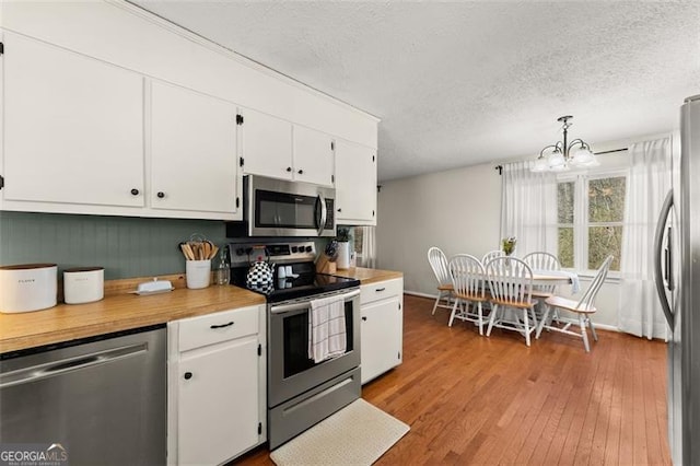 kitchen with light wood-type flooring, a textured ceiling, white cabinetry, appliances with stainless steel finishes, and light countertops