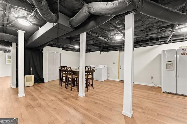 finished basement with light wood-style flooring, washer / clothes dryer, baseboards, and white fridge with ice dispenser