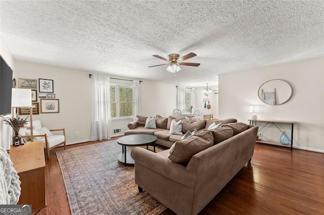 living area with ceiling fan with notable chandelier, wood finished floors, baseboards, and a textured ceiling