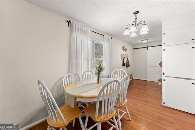 dining area with a barn door, light wood-style flooring, a notable chandelier, and a textured ceiling