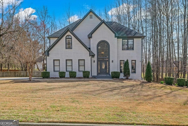 french provincial home with brick siding, a front lawn, and fence