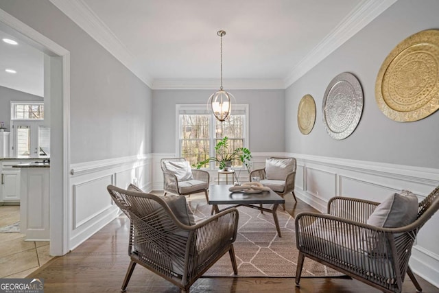 sitting room featuring crown molding, wainscoting, light wood finished floors, and a chandelier