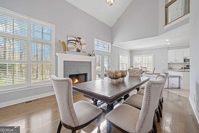 dining area with baseboards, visible vents, high vaulted ceiling, a fireplace, and light wood-type flooring