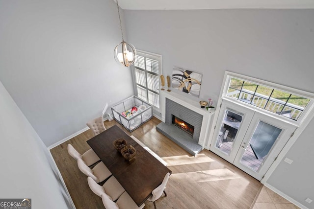 living area with a warm lit fireplace, high vaulted ceiling, baseboards, and wood finished floors