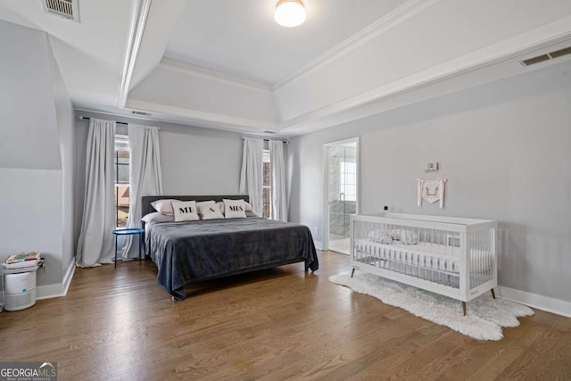 bedroom featuring multiple windows, a raised ceiling, wood finished floors, and ornamental molding