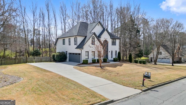 french country home with a front lawn, an attached garage, fence, and driveway