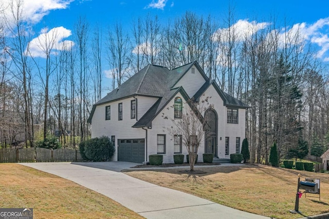 french country home with a front yard, fence, an attached garage, concrete driveway, and brick siding