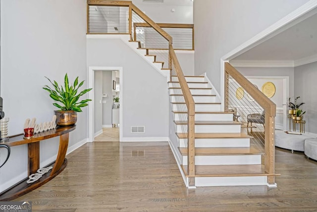 stairs featuring visible vents, wood finished floors, crown molding, baseboards, and a towering ceiling