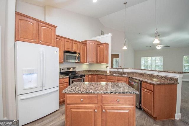 kitchen with dark stone countertops, a kitchen island, a peninsula, a sink, and appliances with stainless steel finishes