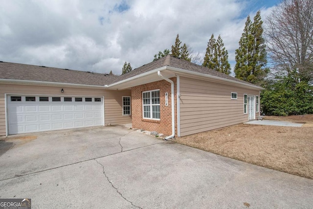 view of side of home with a garage, brick siding, roof with shingles, and concrete driveway