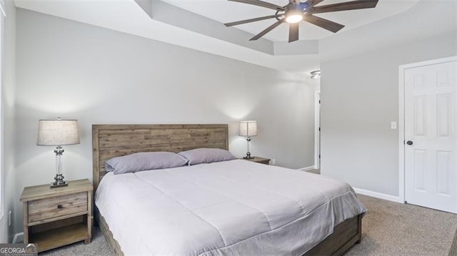 carpeted bedroom with a tray ceiling, baseboards, and ceiling fan