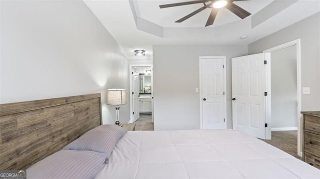 carpeted bedroom featuring a tray ceiling, a ceiling fan, and connected bathroom